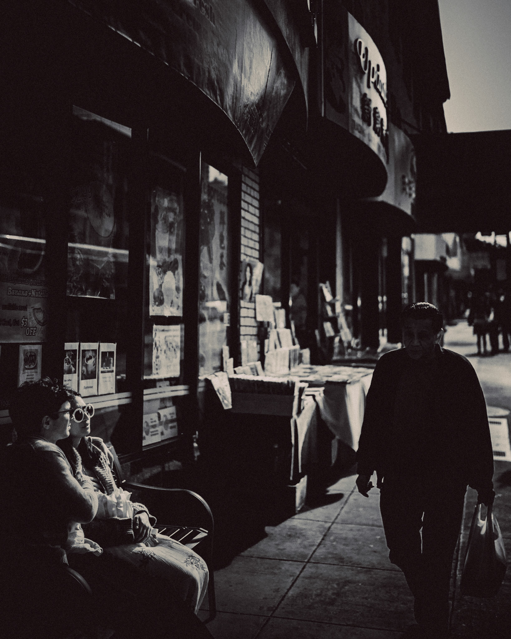 A black and white photo of couple on a bench, with an old Asian man walking by. Chinatown, San Francisco, California, USA, June 2016, Leica M.