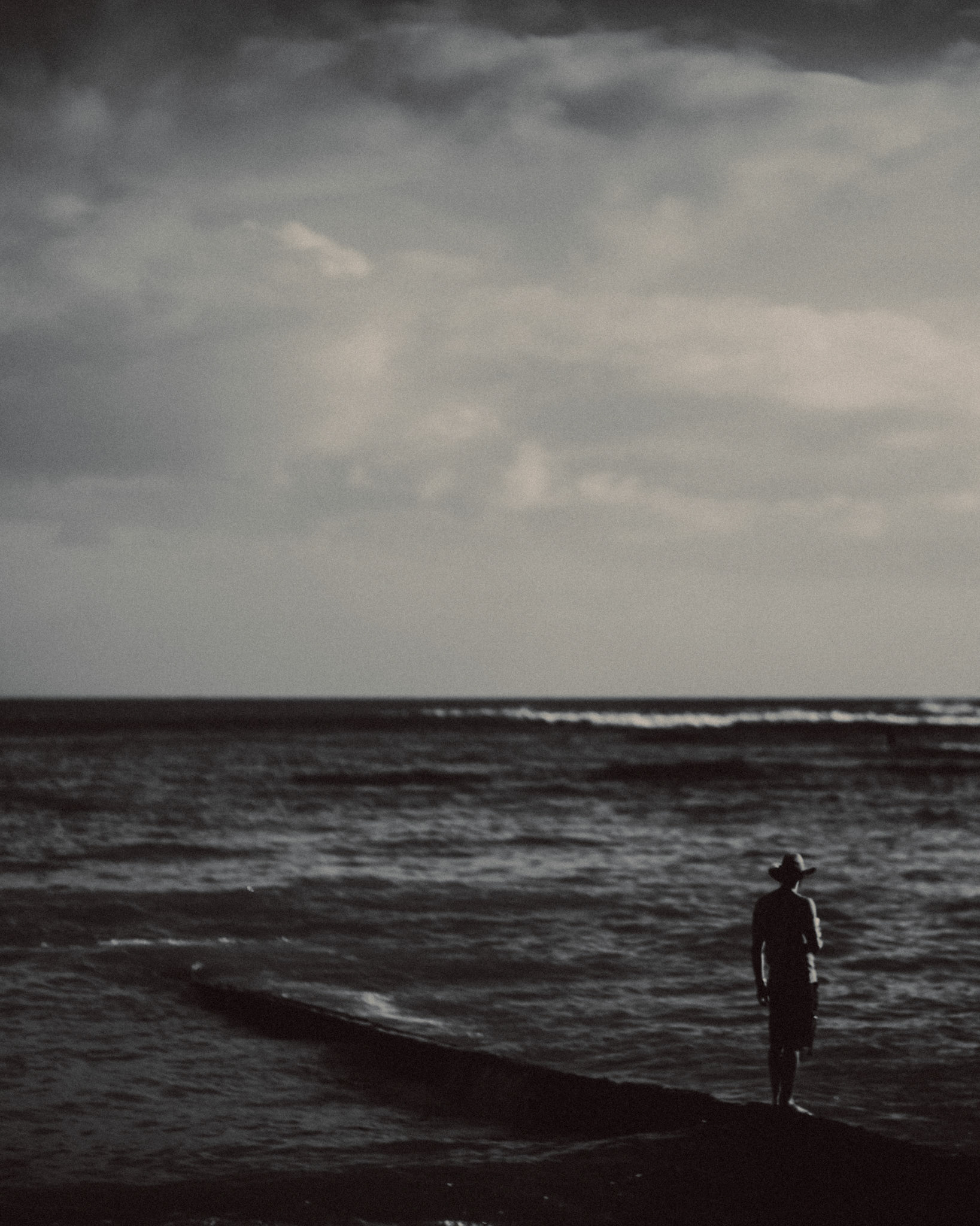A man standing on a breakwater in Waikiki Beach, in black and white, Honolulu, Hawaii, USA, September 2015, iPhone 6 Plus.