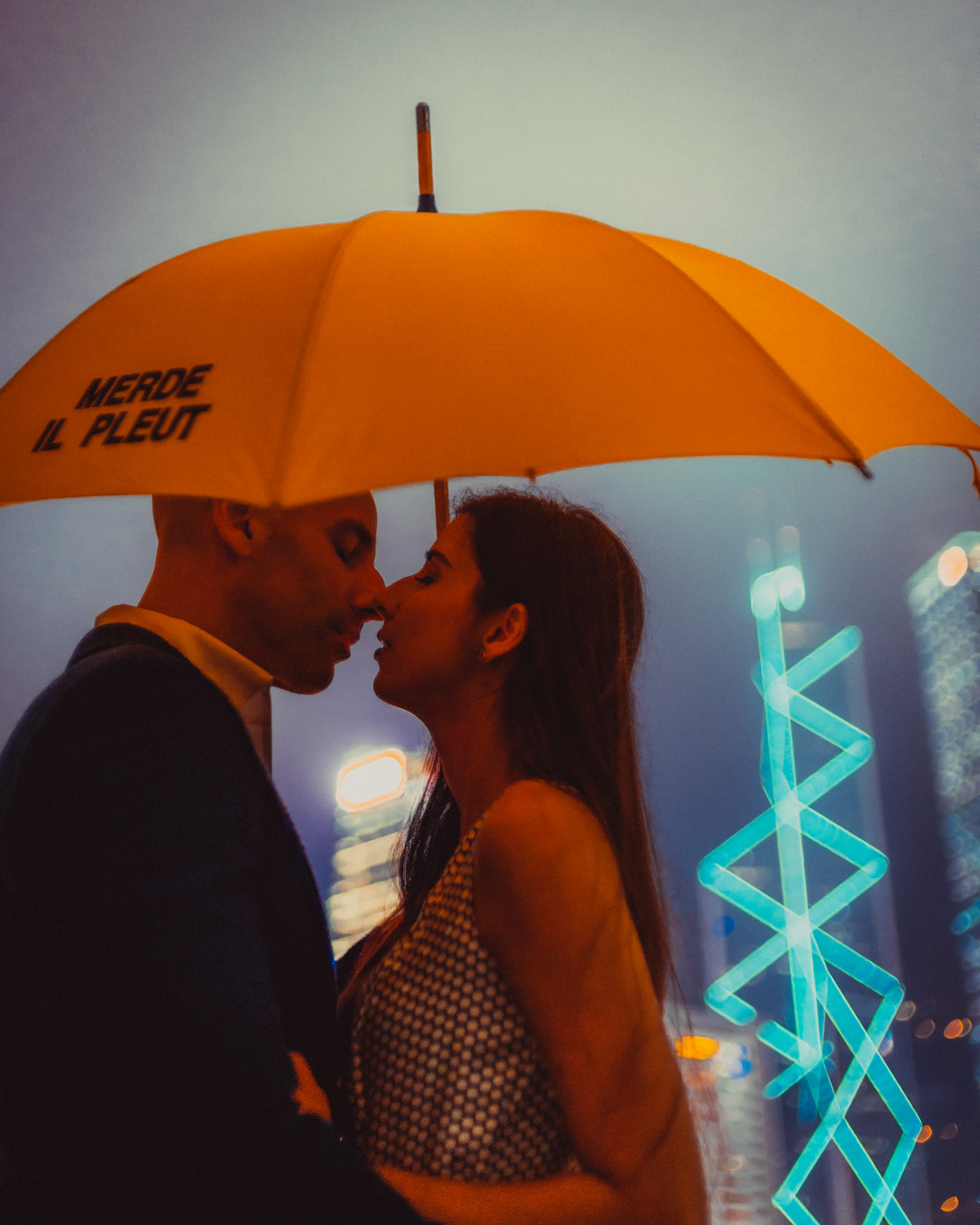 A moody and intimate late night urban engagement shoot with the couple under a bright yellow Merde Il Pleut umbrella and the Bank of China tower in the backgroun, from Eric and Sabrina's prewedding shoot in Central, Hong Kong, April 2019, Sony A7III.