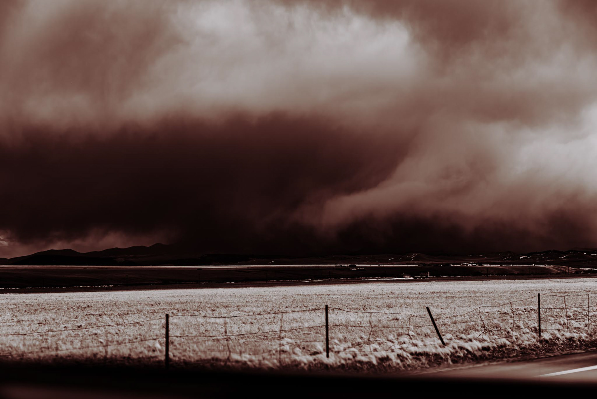 Vintage Black and White image depicting thick clouds over Colorado Rockies mountains, with a fenced area on the back roads of Colorado.