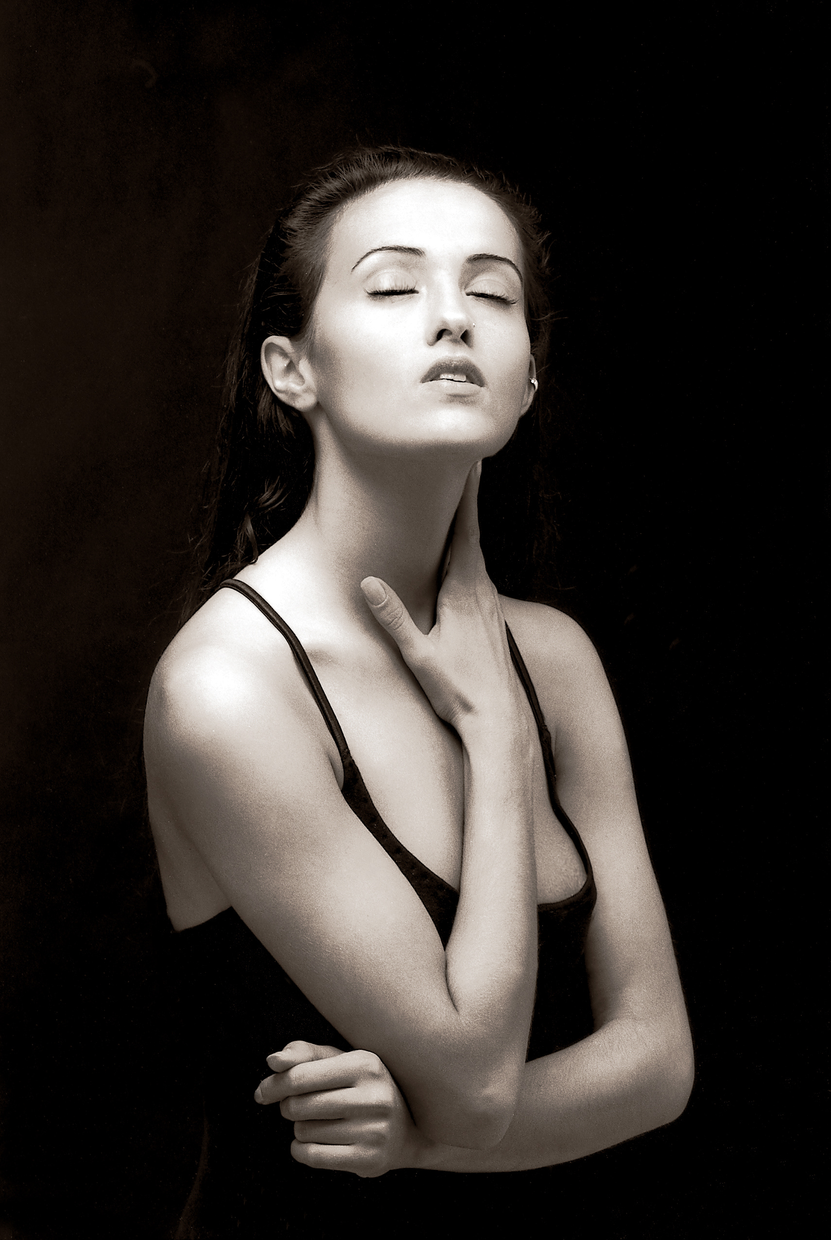 Helin, eyes closed with her hand on her neck against a black background in black and white