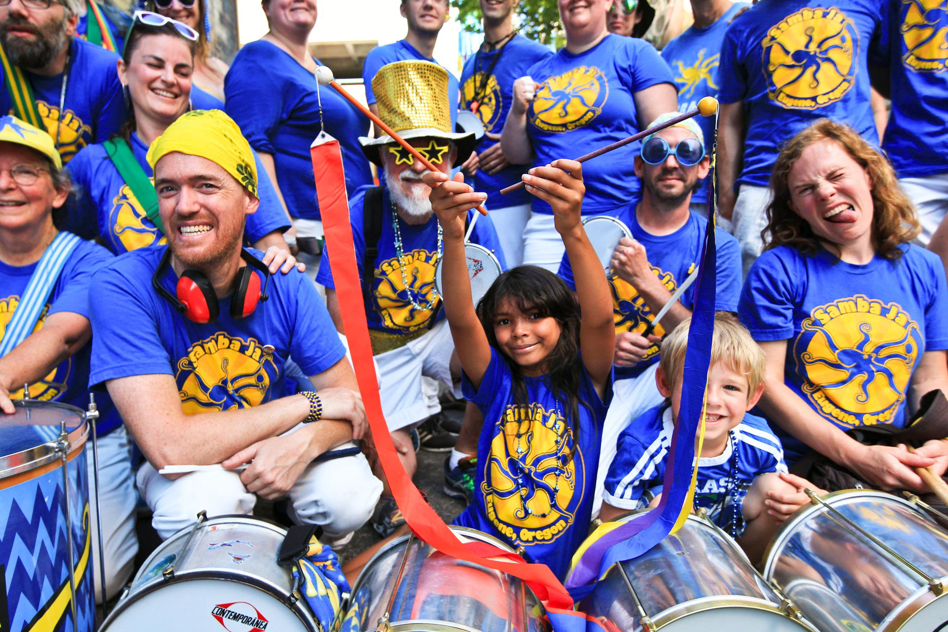 Samba Ja, Eugene community drumming group, gathered for large group photo with young girl in center with batons
