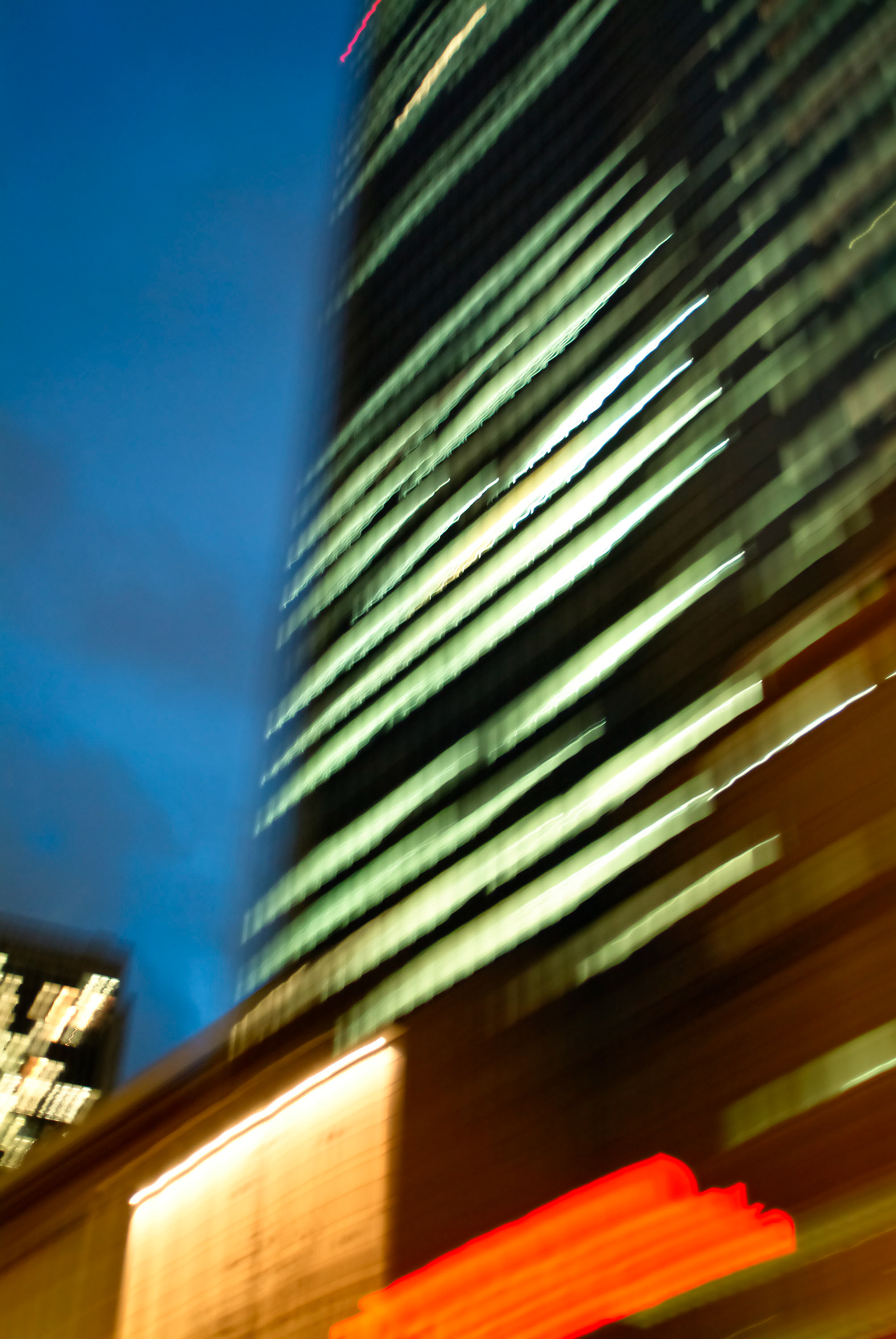 Rush Hour in Frankfurt - Schnell durch die City. Die grüne Welle reiten. Nach oben schauen durch die Windschutzscheibe auf den Büroturm in der Dämmerung. Verschwommene Fassade mit hellen Lichtstreifen. Dahinter Maschinen mit Menschen, die große Zahlen mit Lichtgeschwindigkeit um den Globus jagen.
