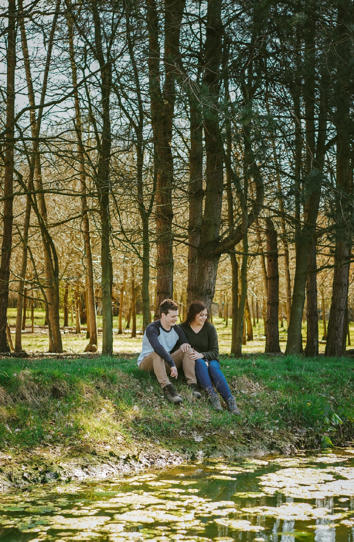 couple sat on bank of lake at endeavour woodland wedding venue in buckinghamshire during pre wedding engagement photo session with david lefebvre a photographer from milton keynes