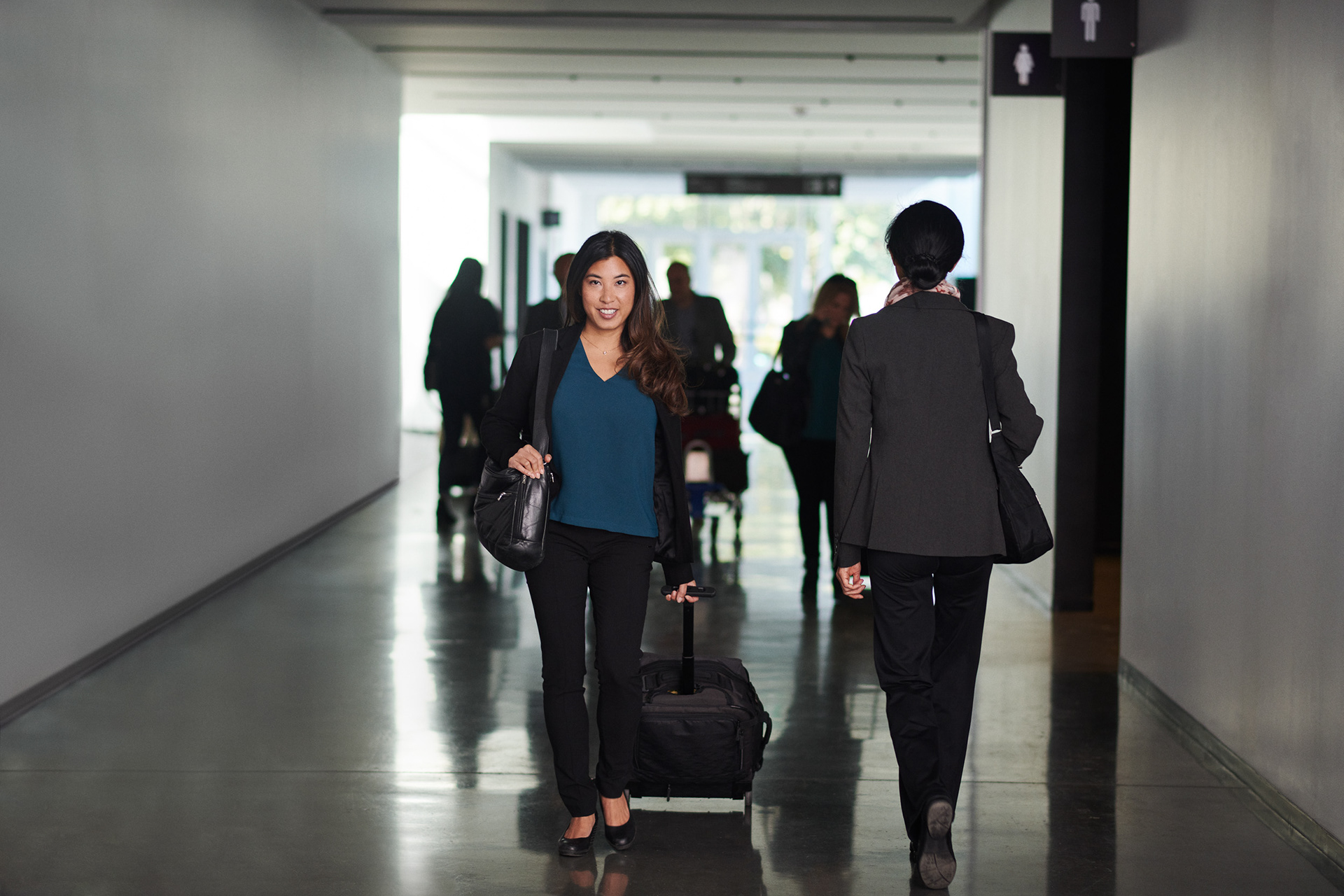 asian woman walking though a photography set designed to look like an airport. she looks up to the camera while passing another traveller heading to her gate.