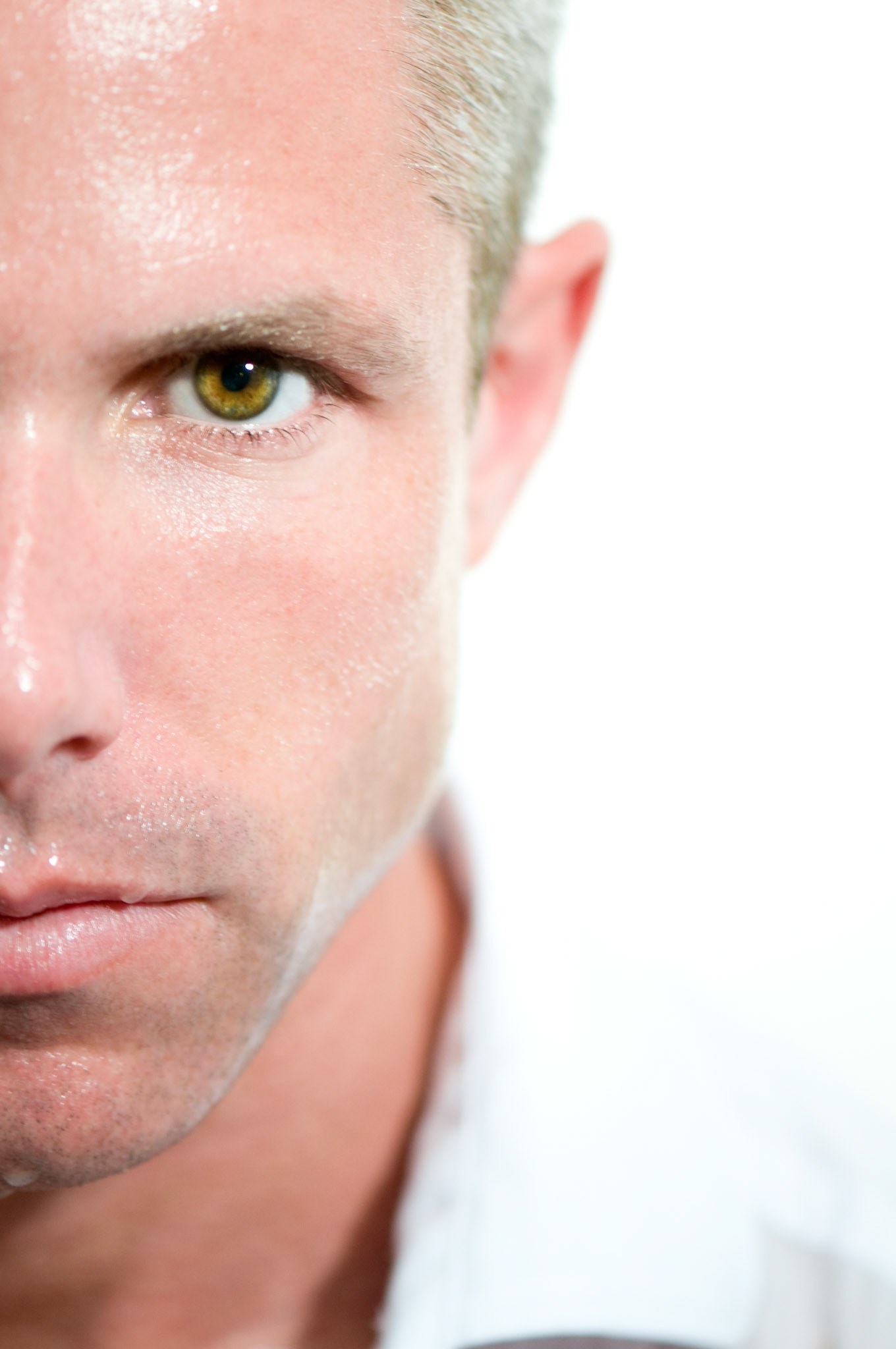 Swetty man looking serious and staring at the camera. Image show half his face with swet dripping from his face. Man is wearing a white shirt, on white background.