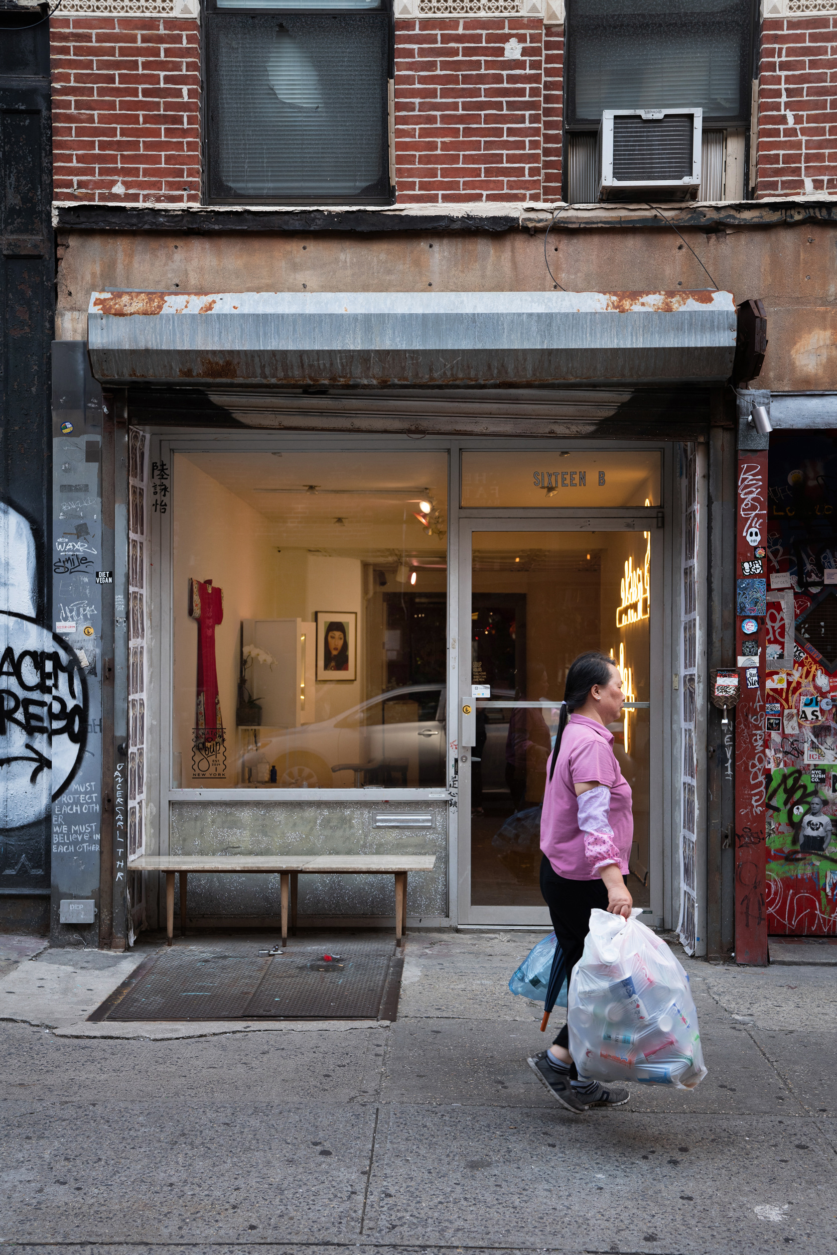 Woman carrying bags of bottles past a city gallery storefront