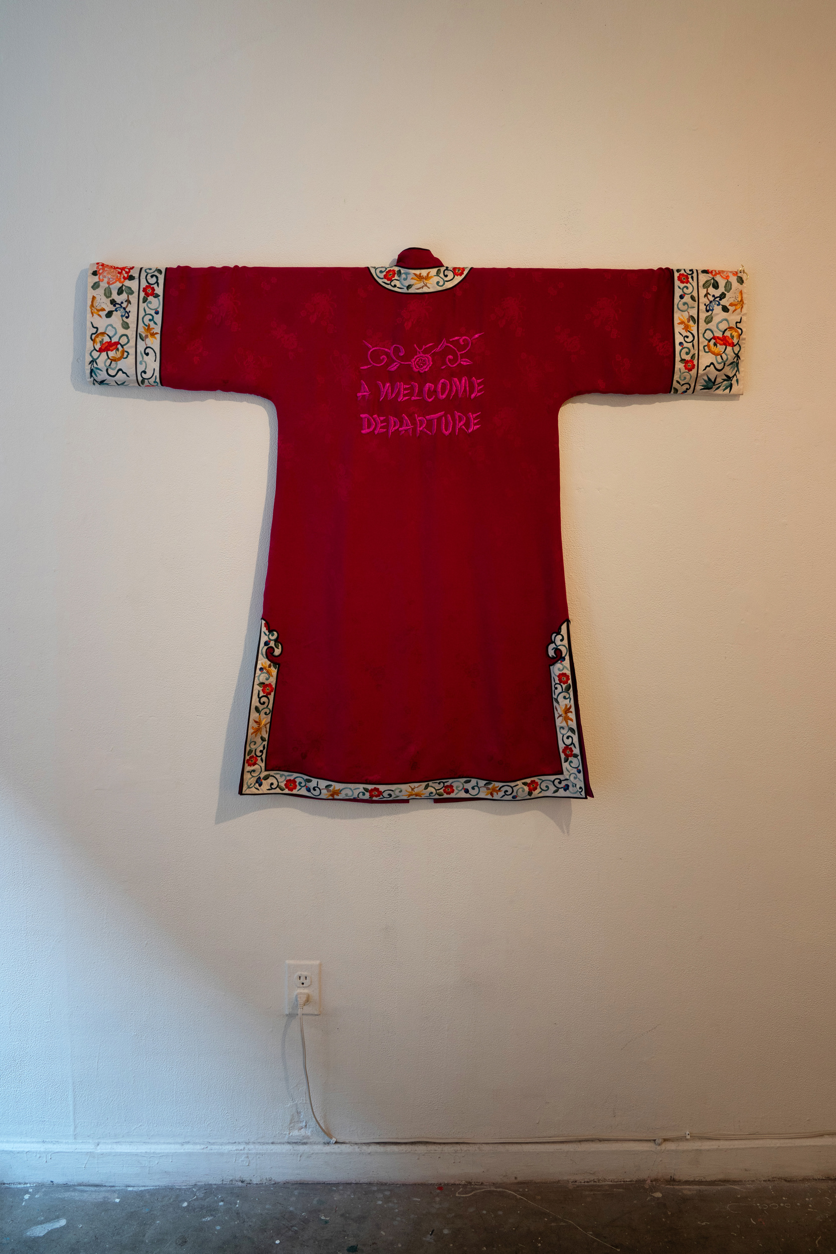 An Asian silk robe with text embroidered that says A WELCOME DEPARTURE