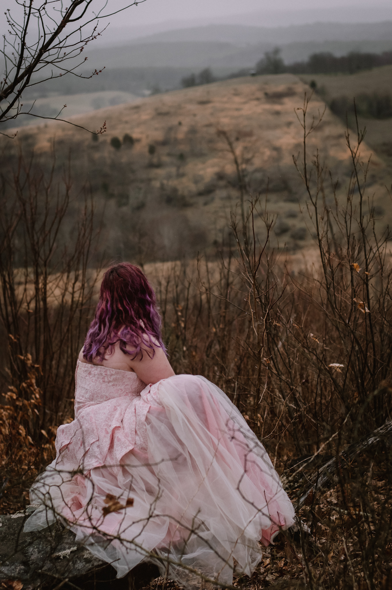 I am sitting down on a rock, looking out into the misty farm fields.
