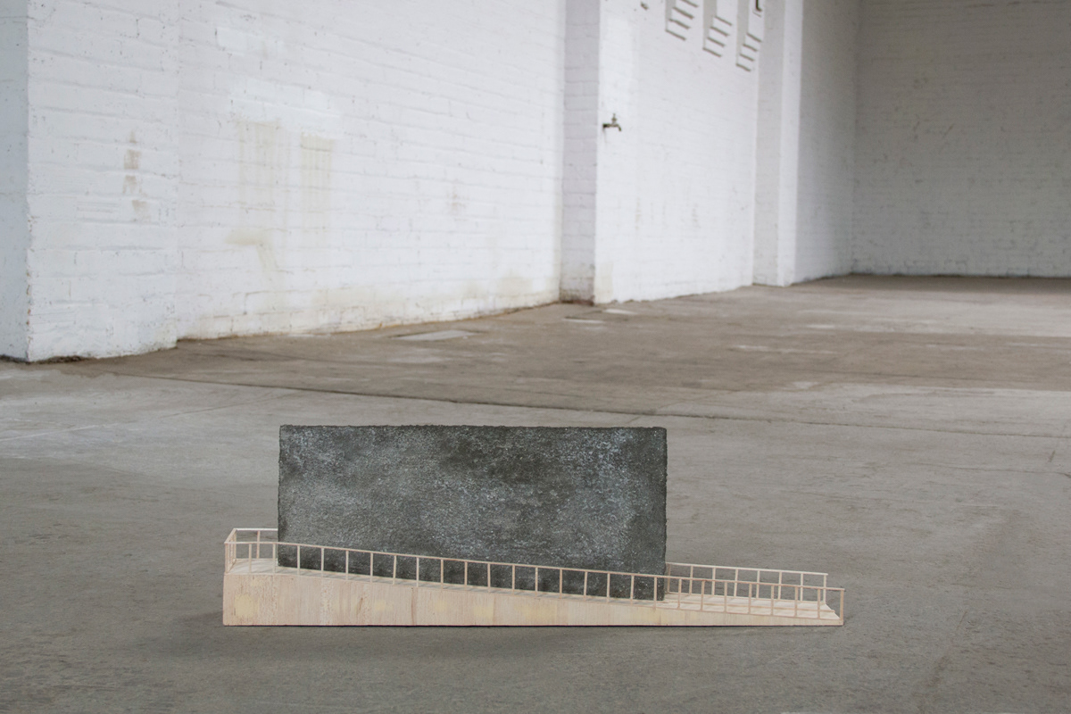 http://Balsa wood model using concrete separation wall with a ramp climbing up one side, around, and back down. The model sits on a concrete floor with a large industrial space in the background.