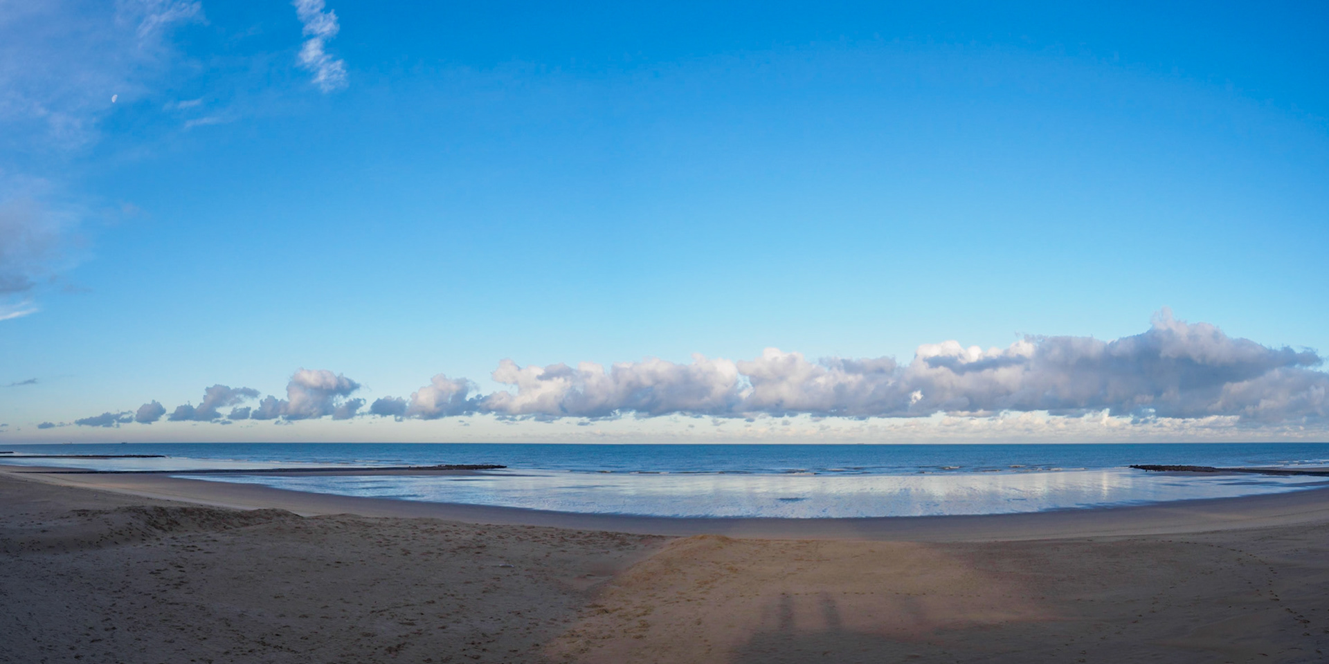 Small moon and train of clouds in a clear sky over North Sea - wide