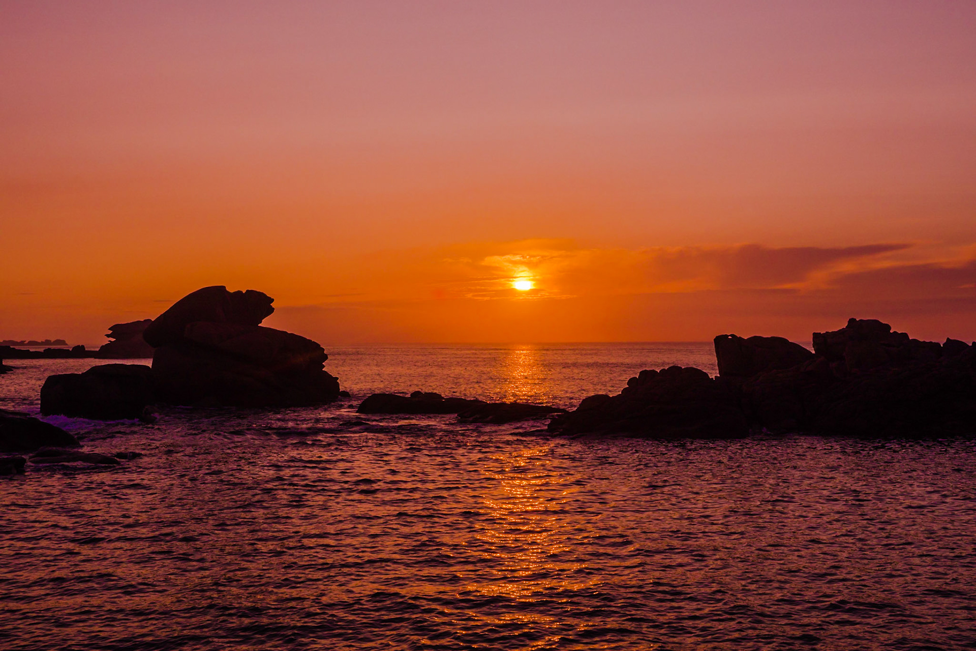The slightly veiled sun setting over the English Channel at Ploumanach, France, reflecting in the water,  casting a soft dim light over the pink granite rocks.