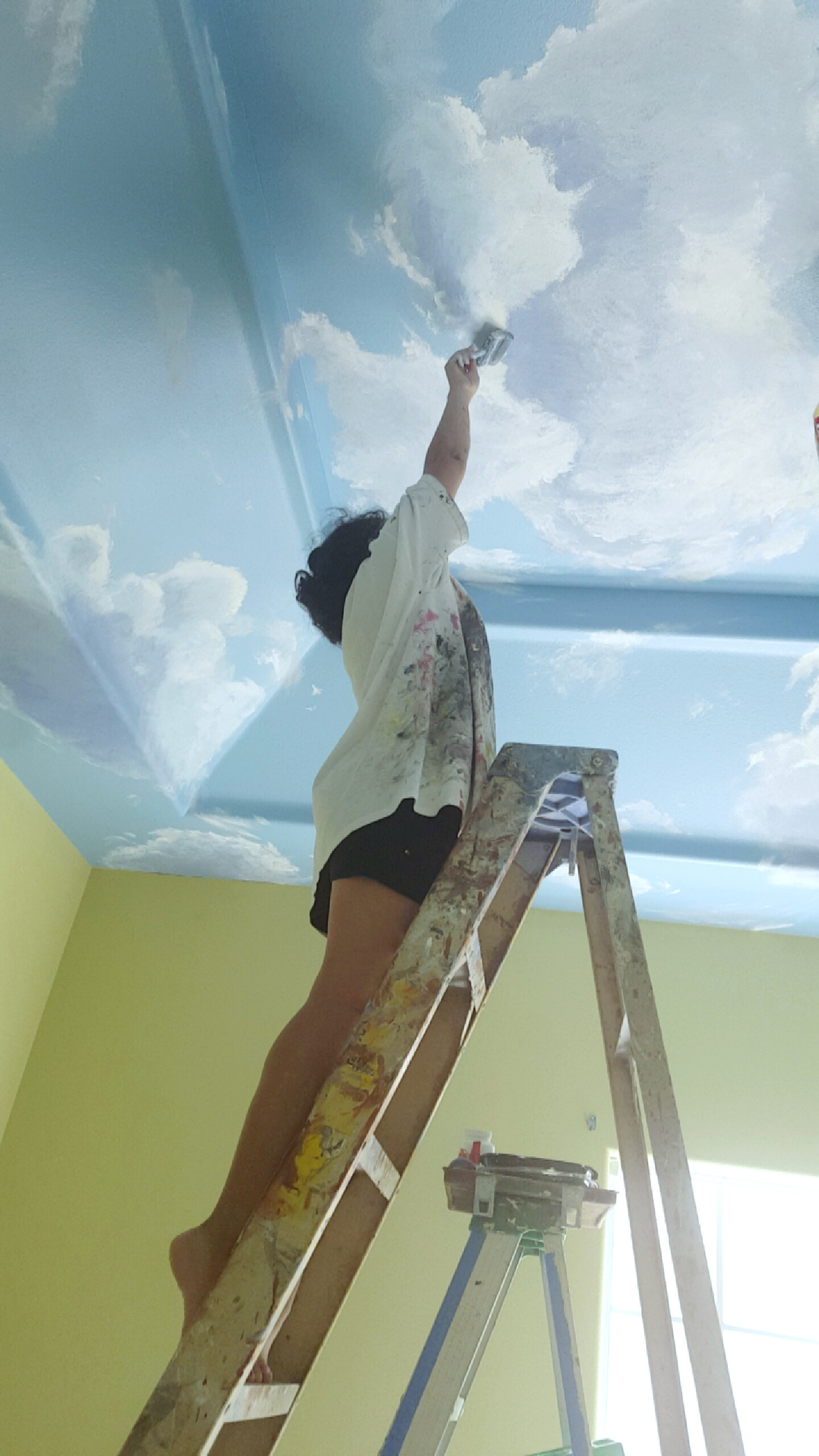 This is an image of Michelle painting a cloudy sky onto her bedroom ceiling.