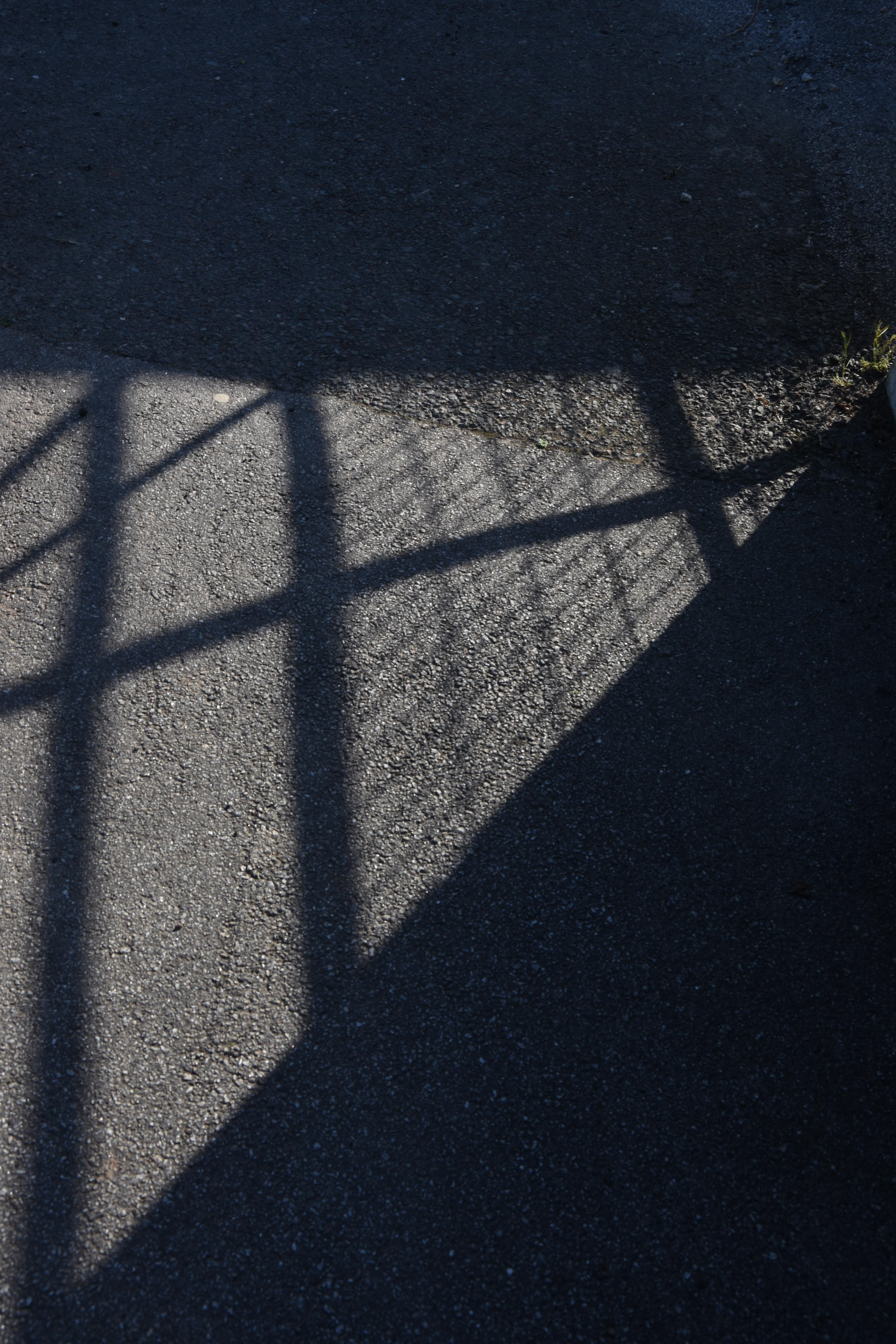 triangle shadow of a gate on the pavement in cornwall by photographer melissa carne